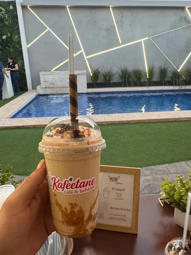 Mano sosteniendo un frappé de cajeta junto a una alberca